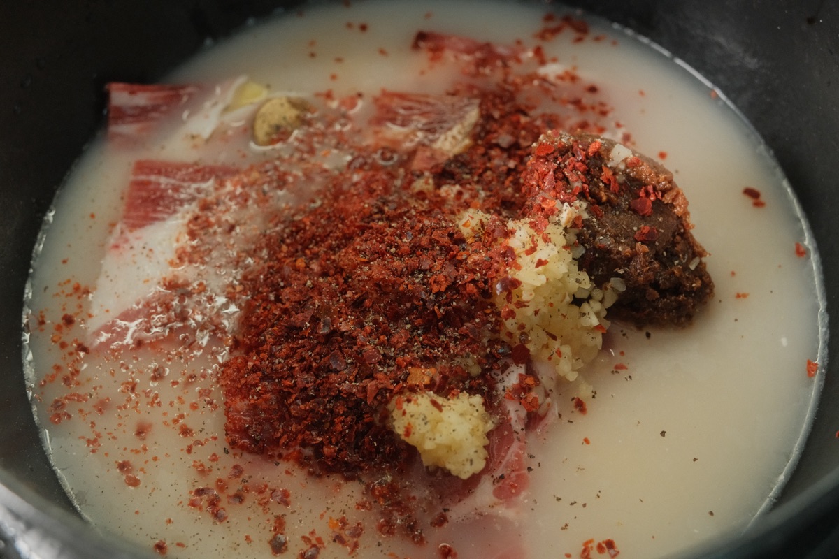Beef slices, gochugaru, doenjang, and garlic in a pot with beef bone broth before cooking