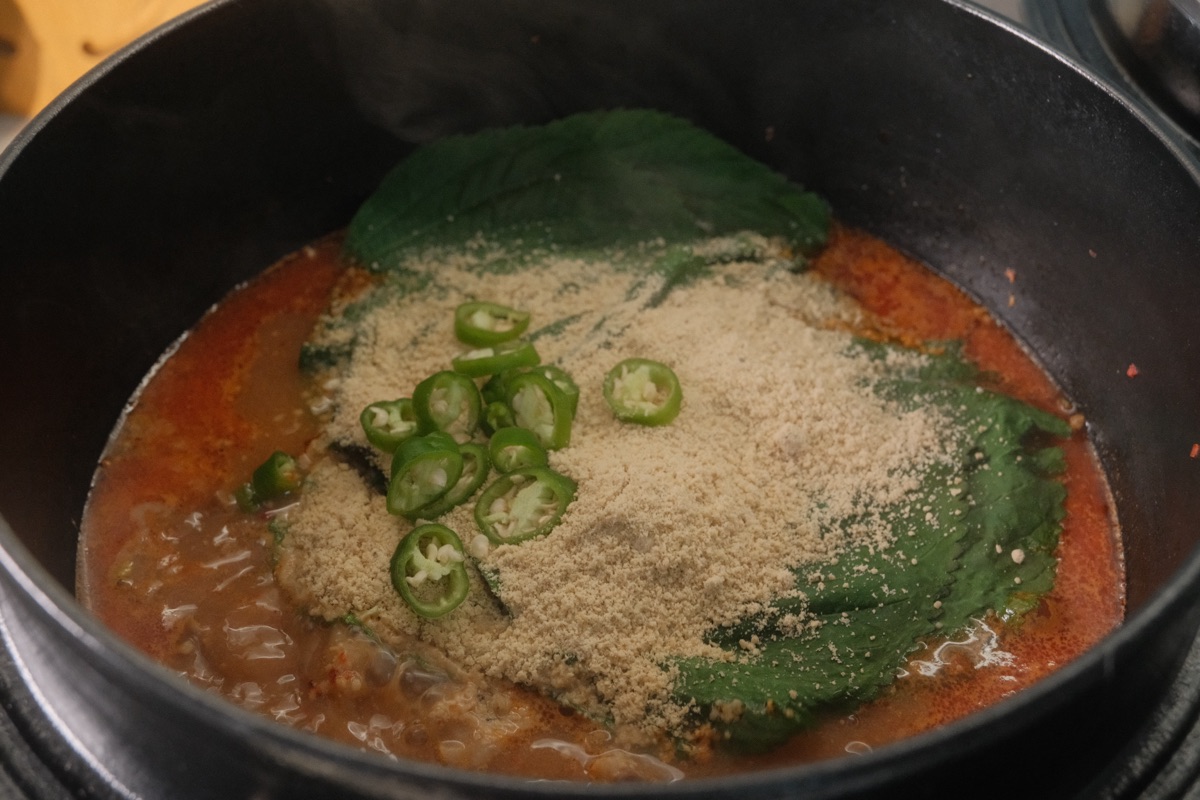 Perilla leaves, perilla seed powder, and sliced green chili added to gamjatang