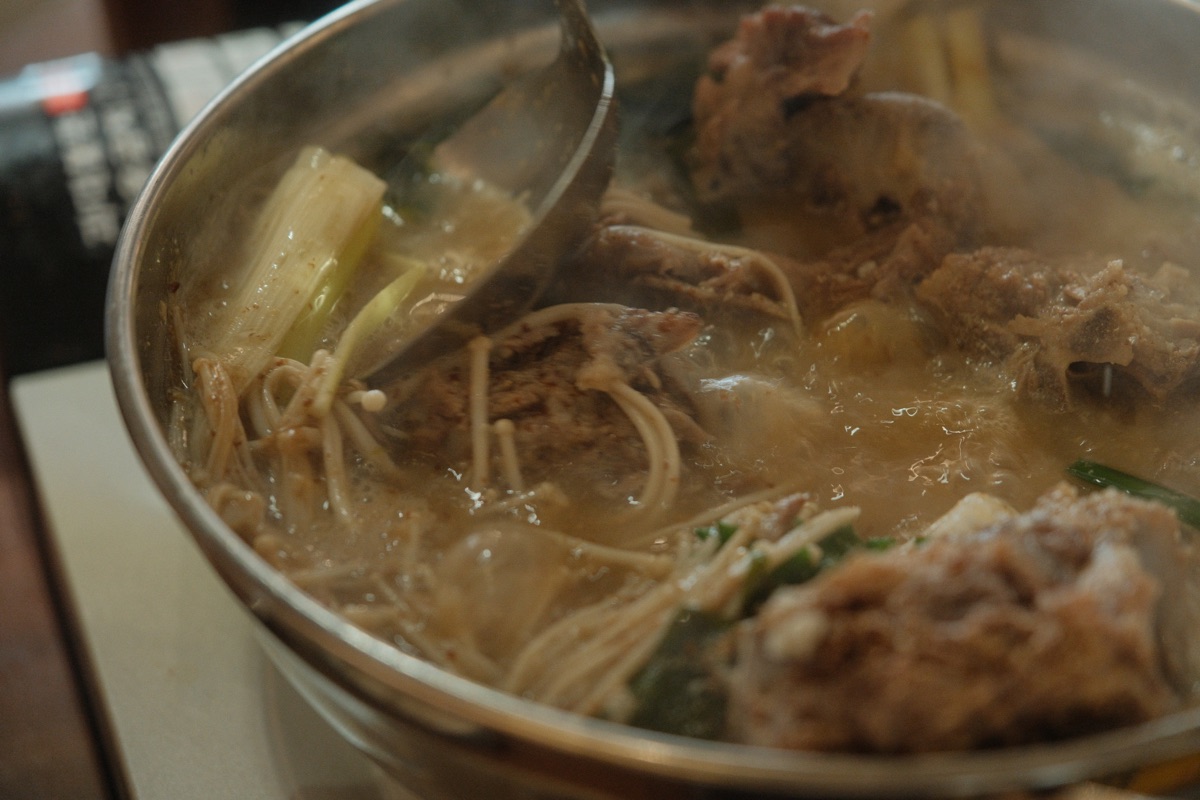 Clear white gamjatang broth simmering with pork bones and vegetables
