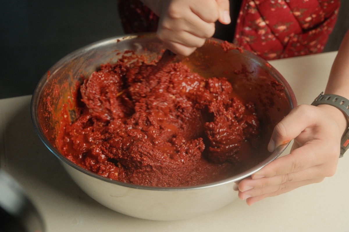 Hands mixing the thick homemade gochujang paste in a stainless steel bowl