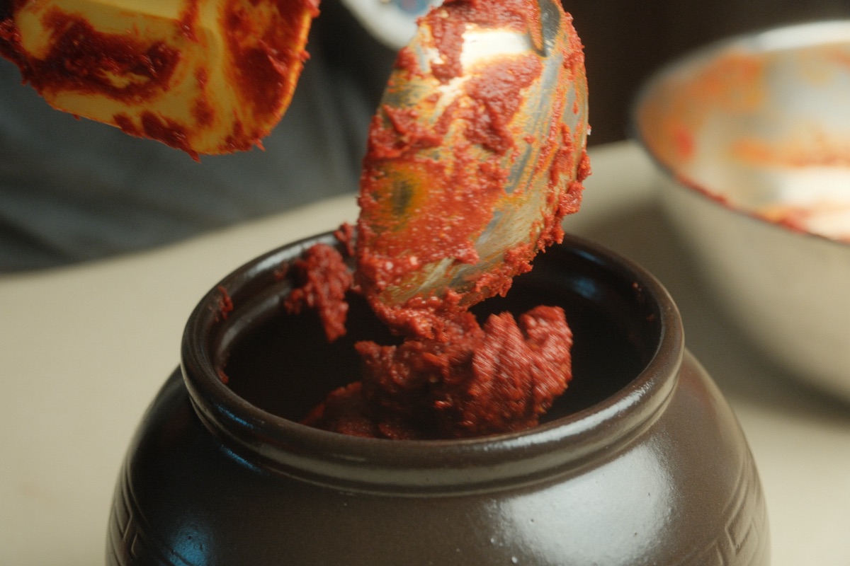 Freshly mixed gochujang being transferred into a brown fermentation jar