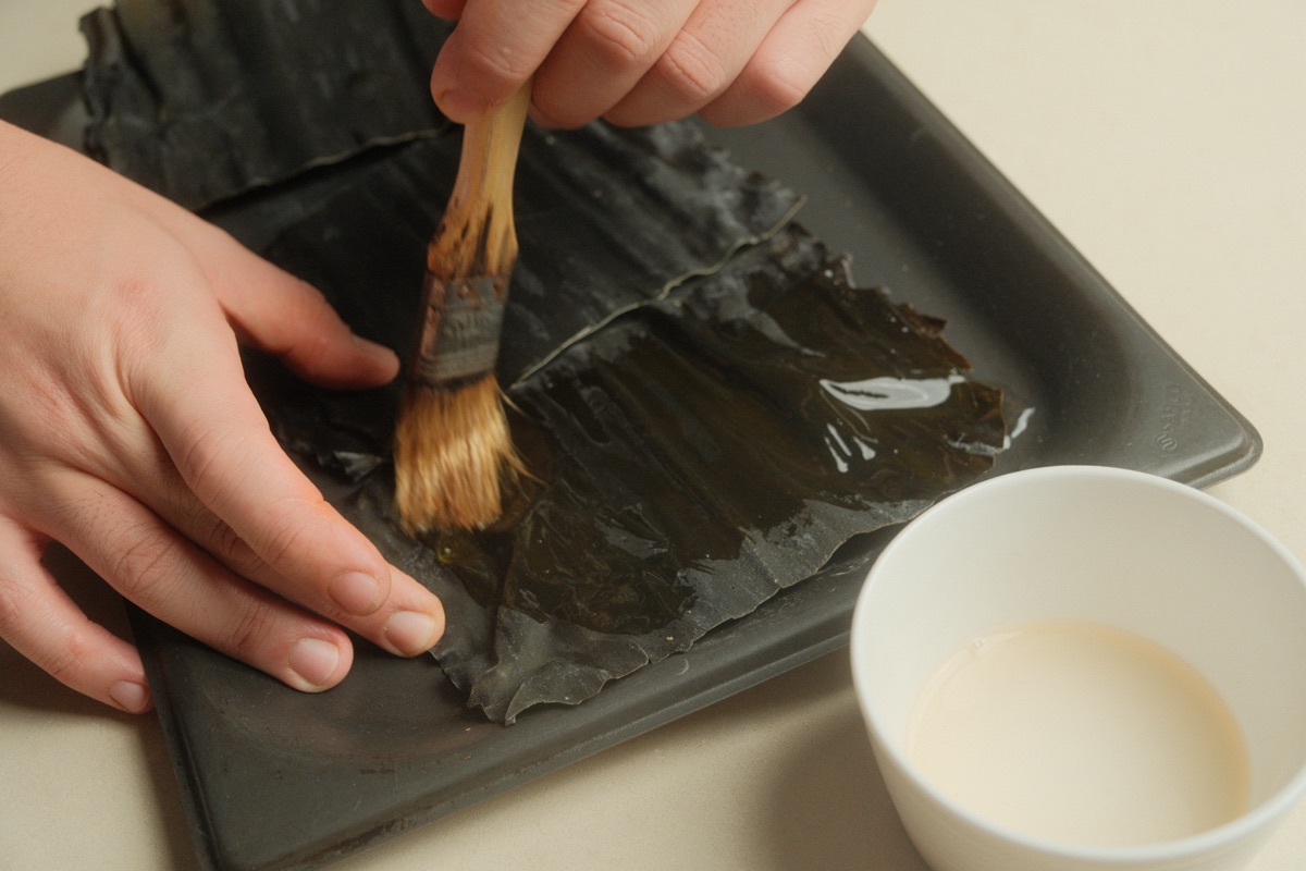 A sheet of dried kelp being brushed with soju before covering the gochujang