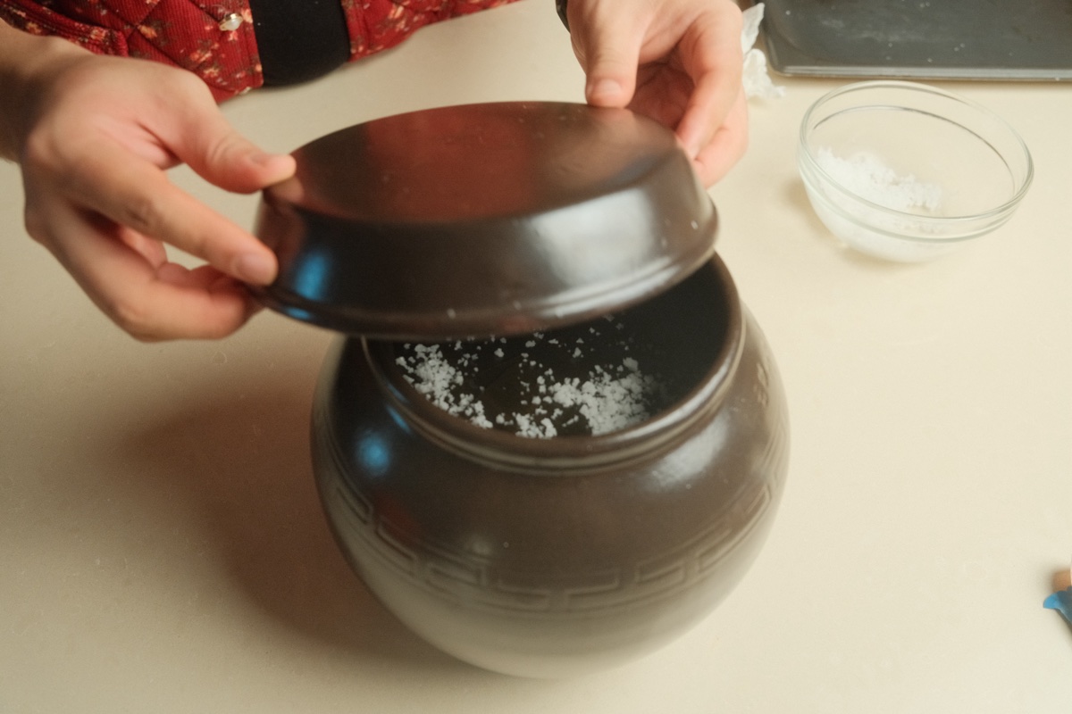 The brown onggi fermentation jar being closed after the gochujang is packed
