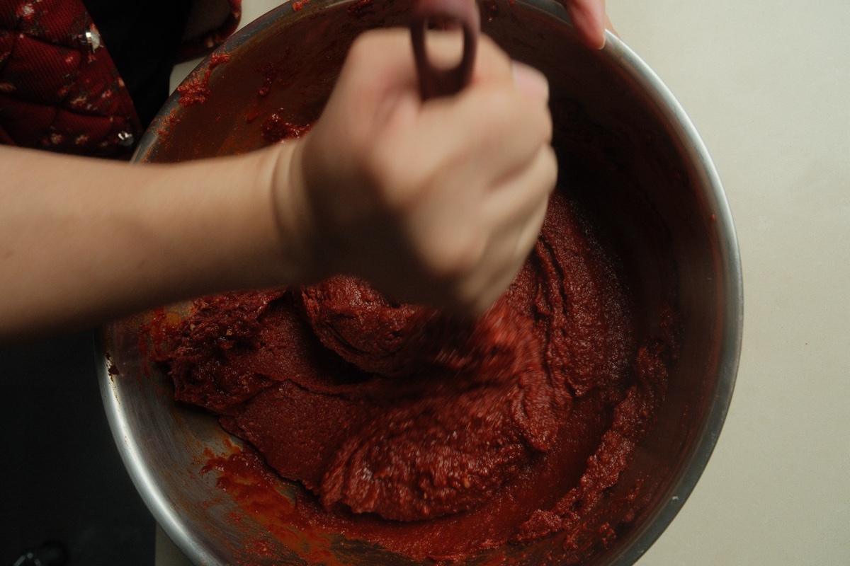 Close-up of the thick red gochujang mixture being worked by hand